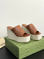 Two Gucci brown leather slide sandals with embossed GG logo and textured espadrille wedge