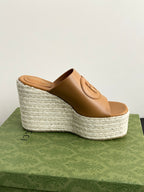 Gucci tan leather slide sandals with raised platform wedge and logo strap detail.