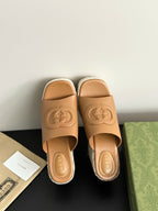 Gucci tan slide sandals showing logos on front straps and white textured platform wedge.