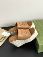 Pair of Gucci tan platform slide sandals with logo on straps and textured white wedge.