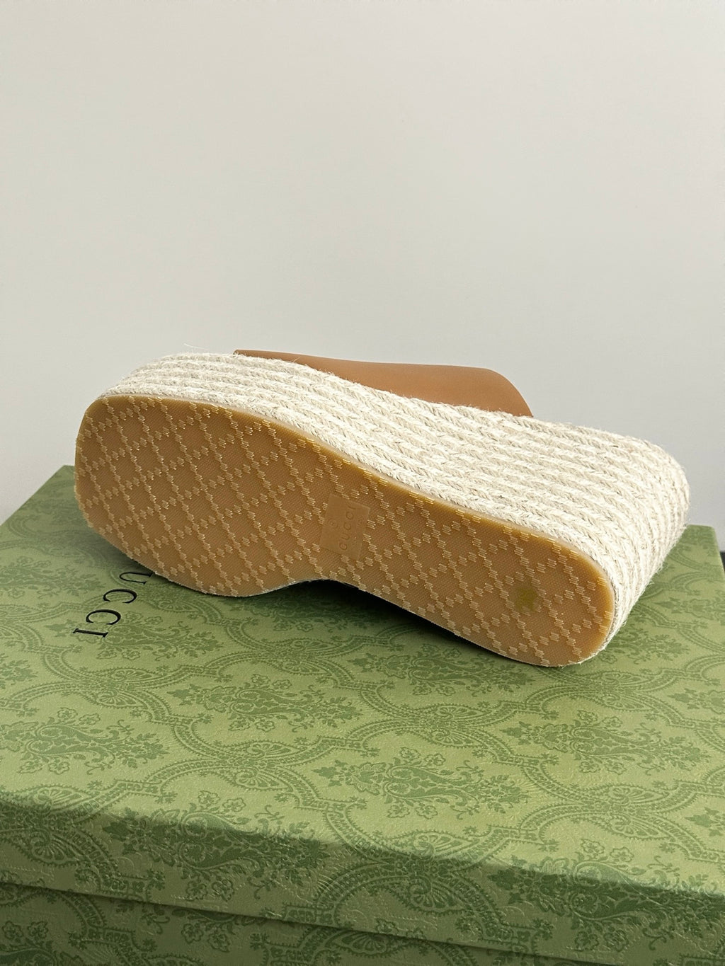 Gucci tan slide sandal outsole on white textured platform wedge, rear angle.