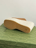 Gucci tan slide sandal outsole on white textured platform wedge, rear angle.