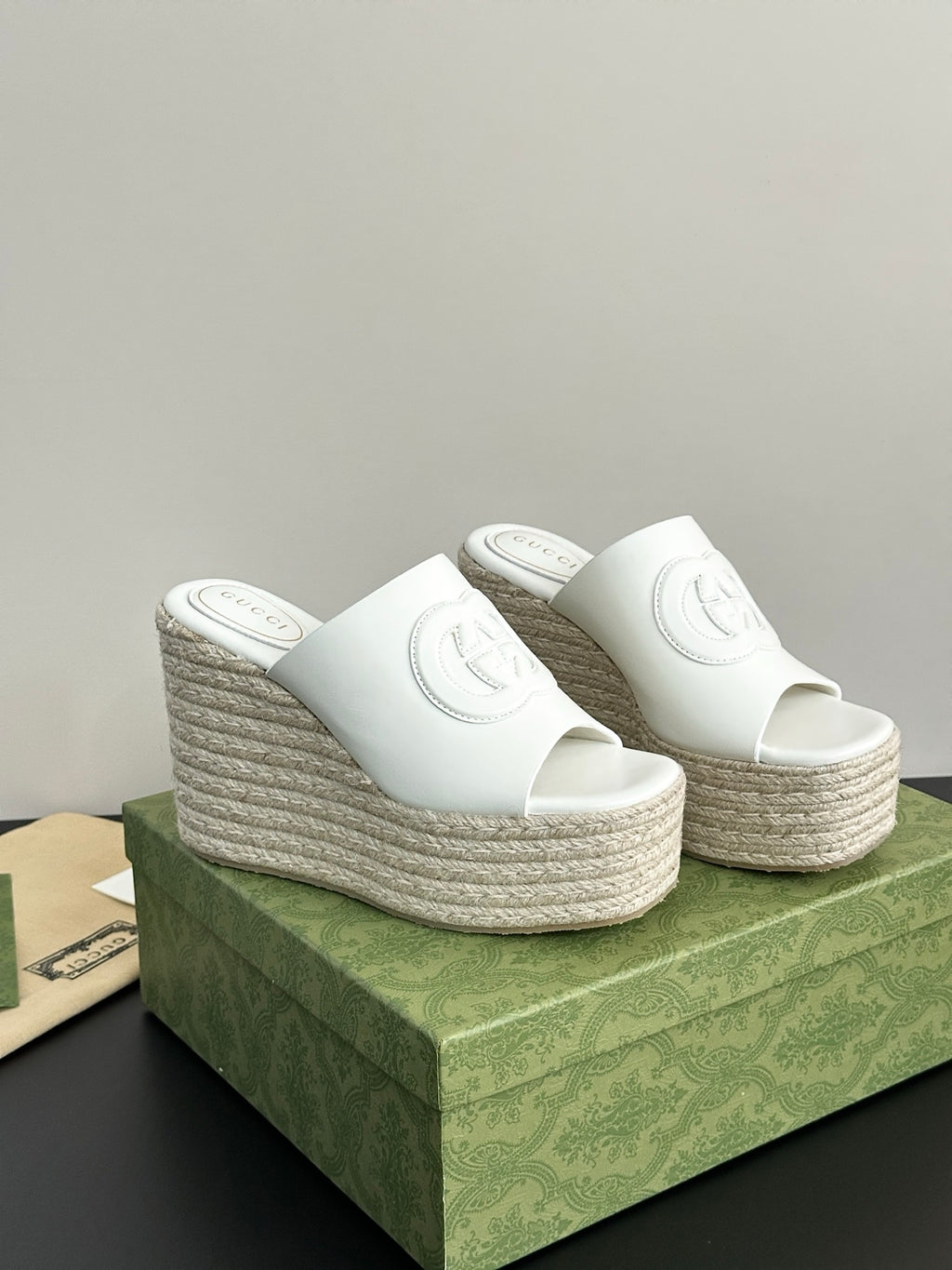 Two white Gucci platform slides with embossed logos and tall woven espadrille wedge