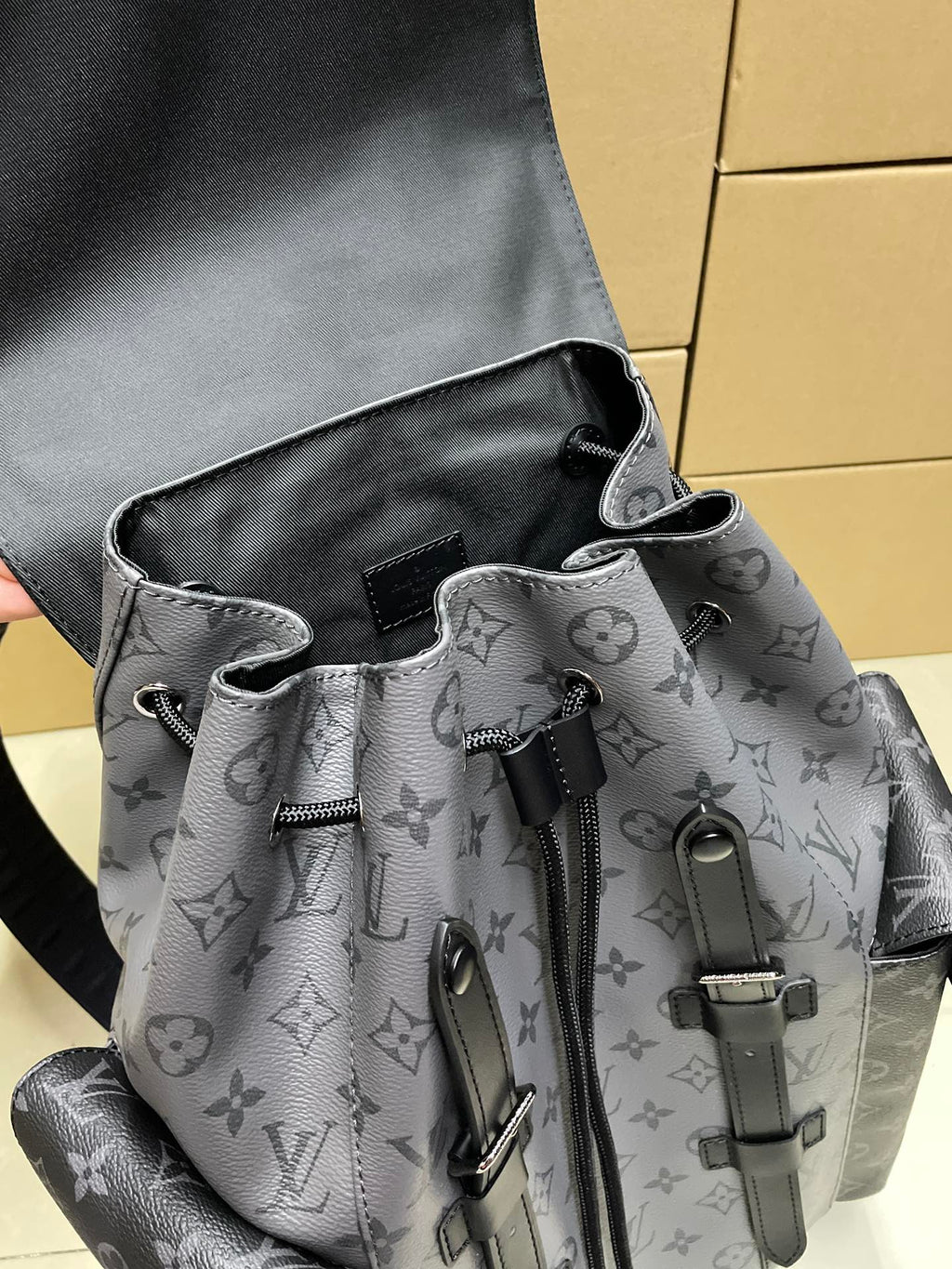 Backpack front view with monogram fabric, drawstring ties, and black hardware clips