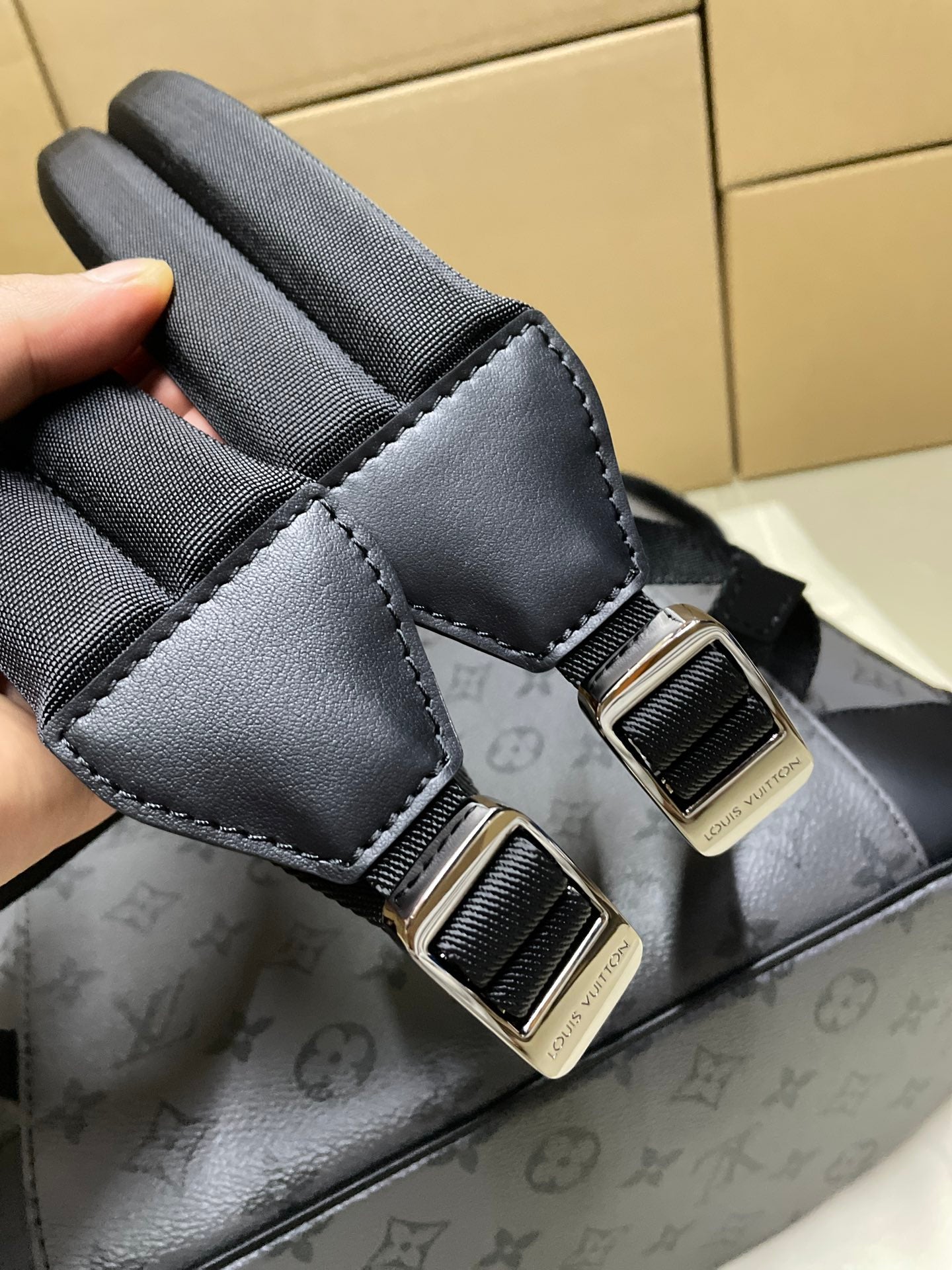 Backpack strap close-up with black adjuster buckle and gray monogram body