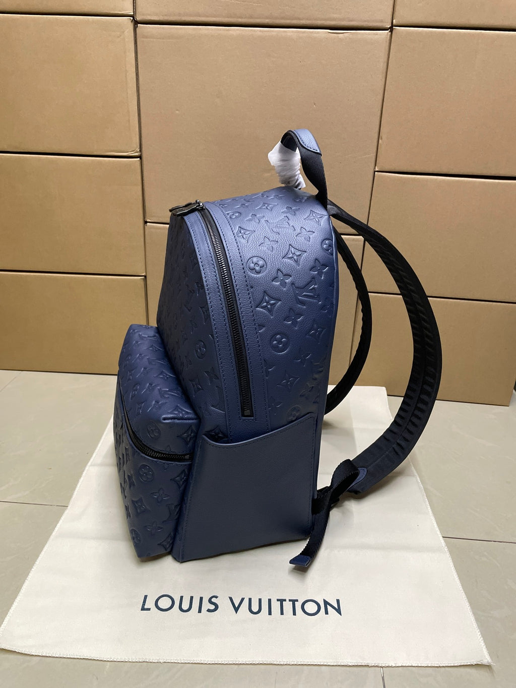Louis Vuitton monogram backpack in navy blue, side view with front zip pocket and strap