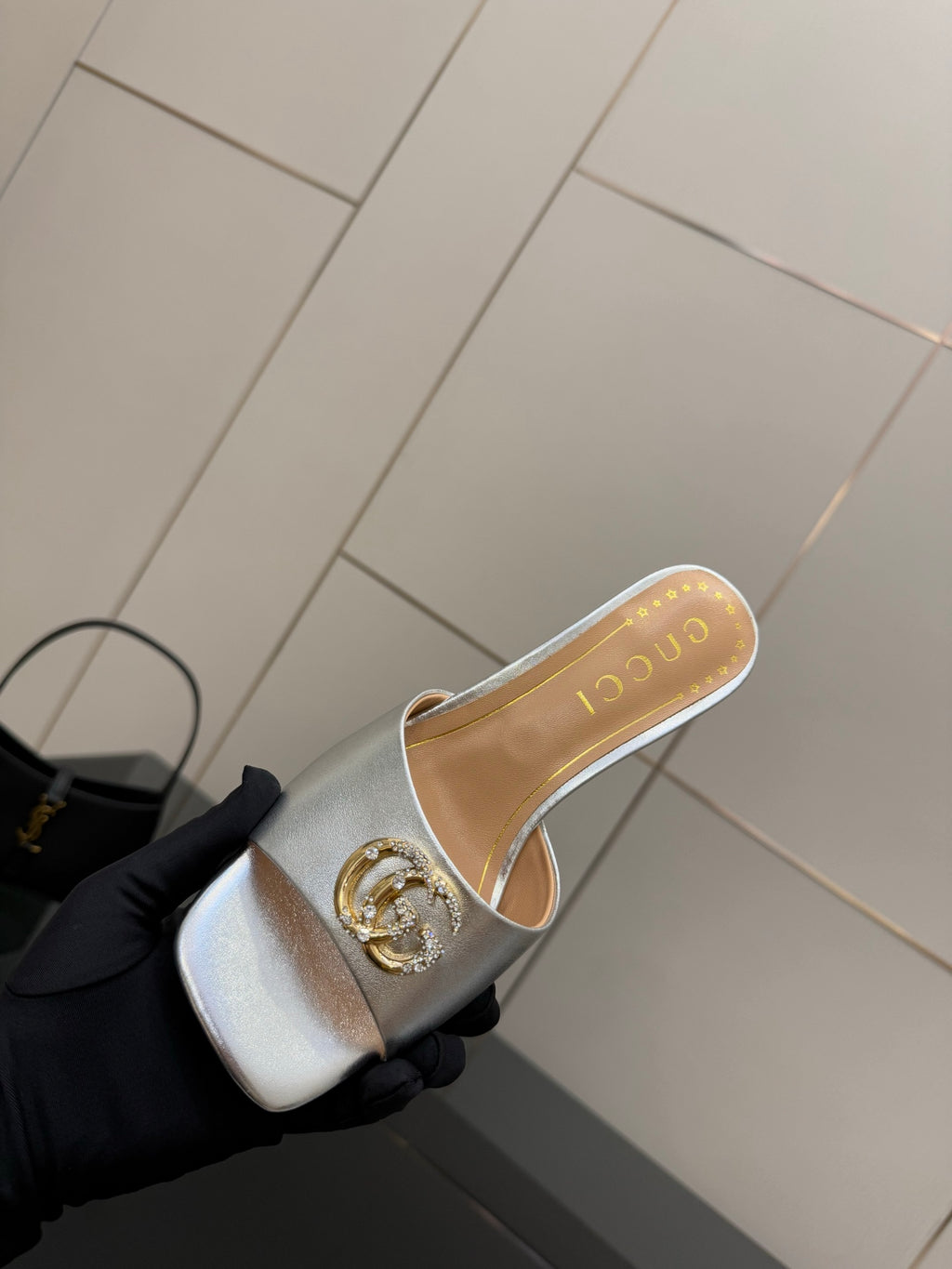 Gucci women's silver mule slide with gold crest ornament on the front strap