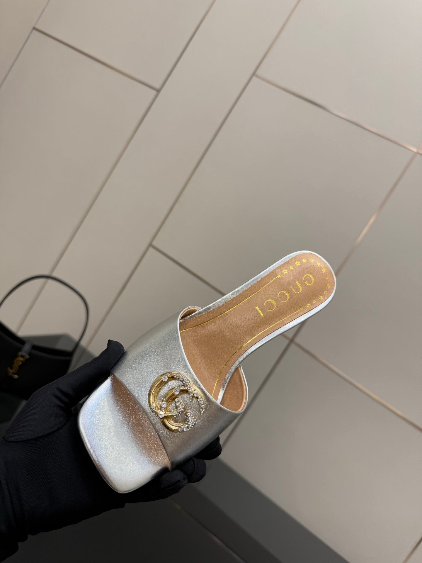 Gucci women's silver mule slide with gold crest ornament on the front strap