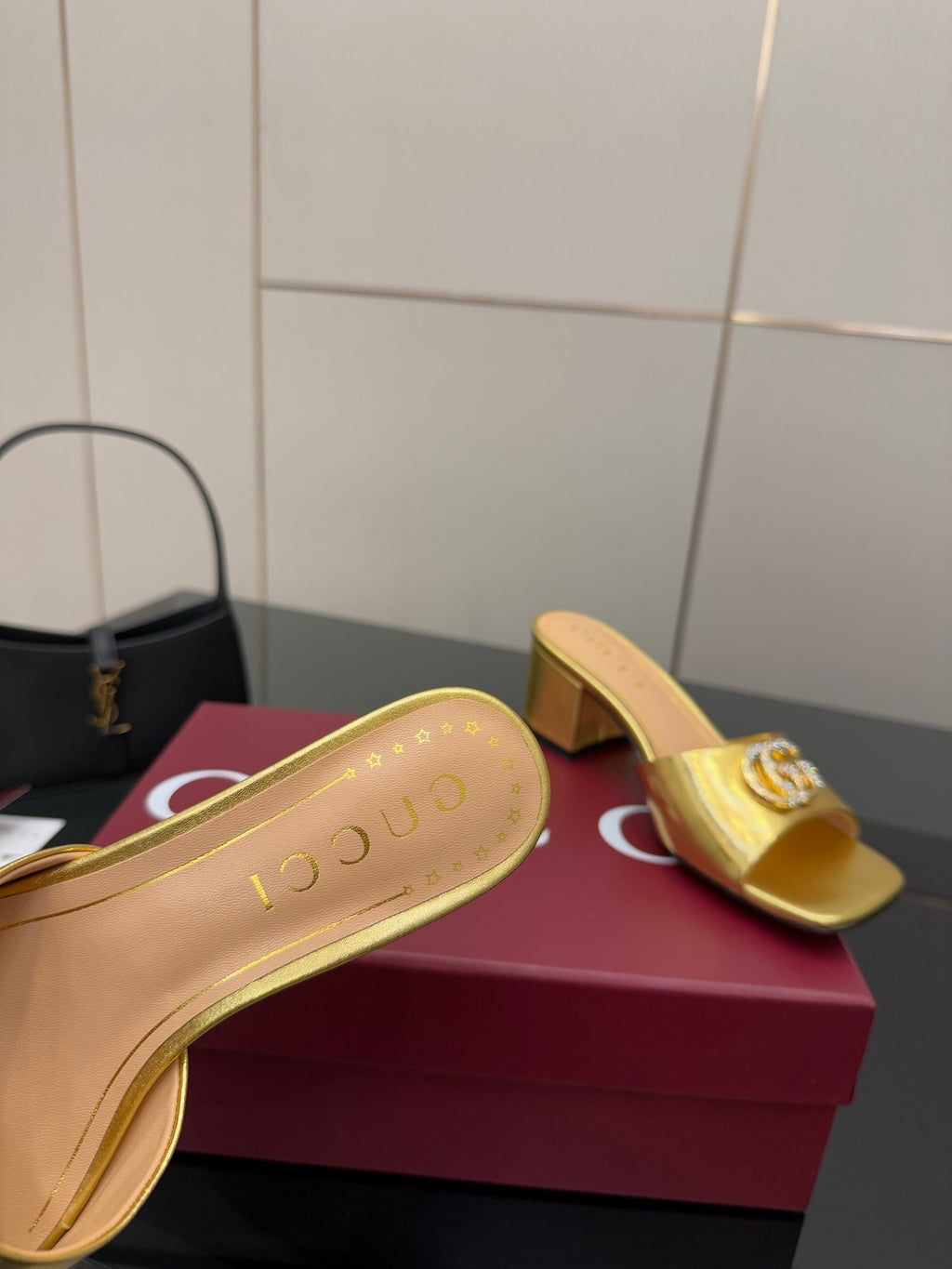 Gucci gold mule soles with printed logo, shown beside matching open-toe slip-ons