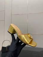 Gucci metallic gold mule on black-gloved hand, open toe and block heel