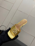 Gucci gold mule on black-gloved hand, showing embossed emblem and open toe