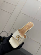 Gucci ladies cream mules with gold-tone logo buckle, angled top view