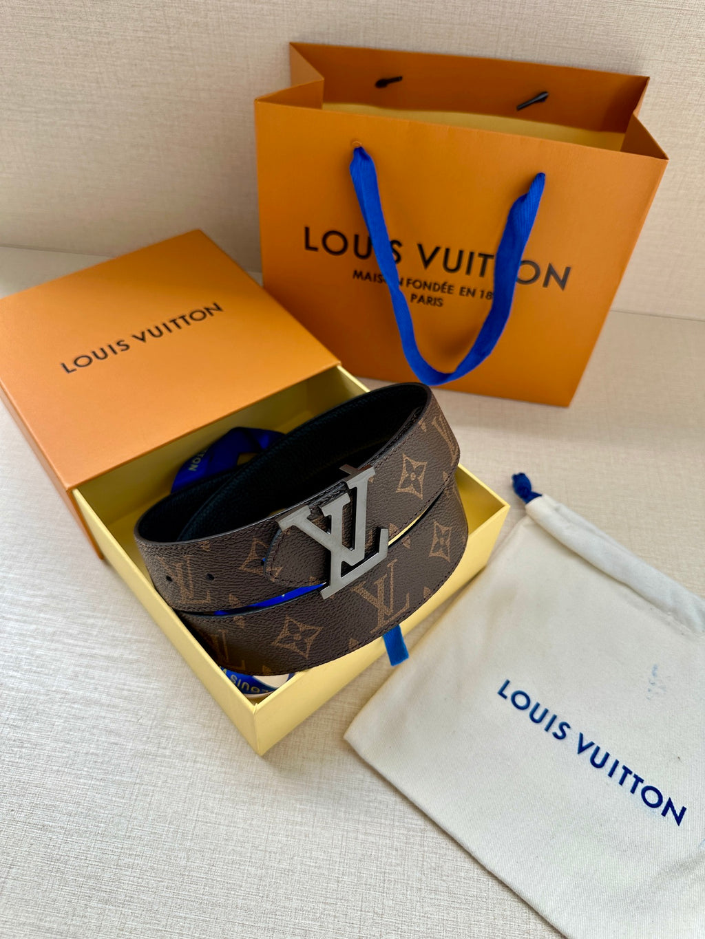Monogram belt with gold buckle resting in open gift box with dust bag