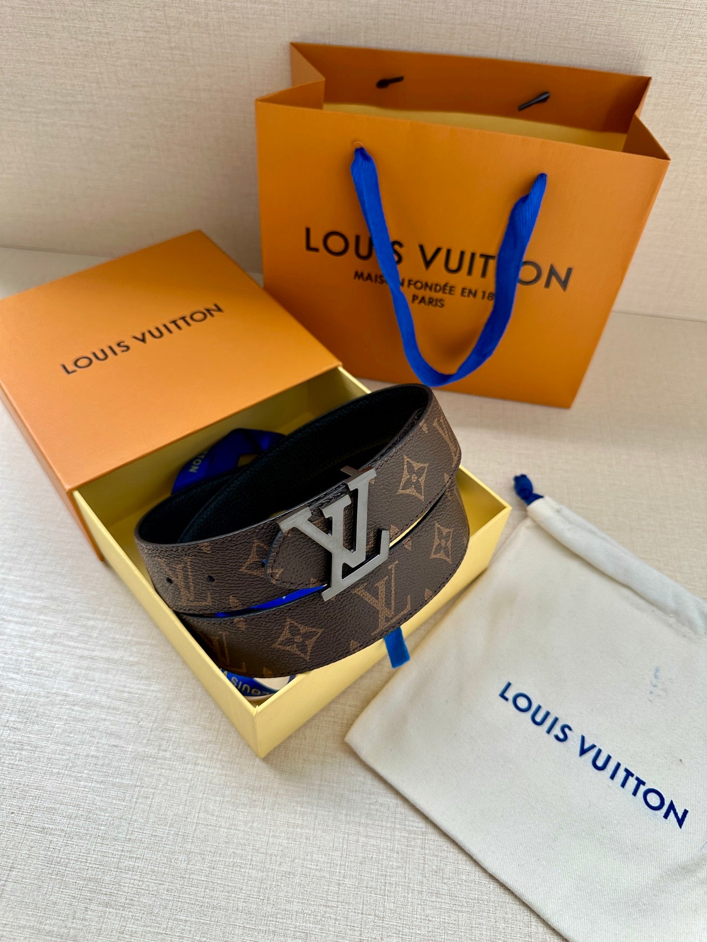 Monogram belt with gold buckle resting in open gift box with dust bag