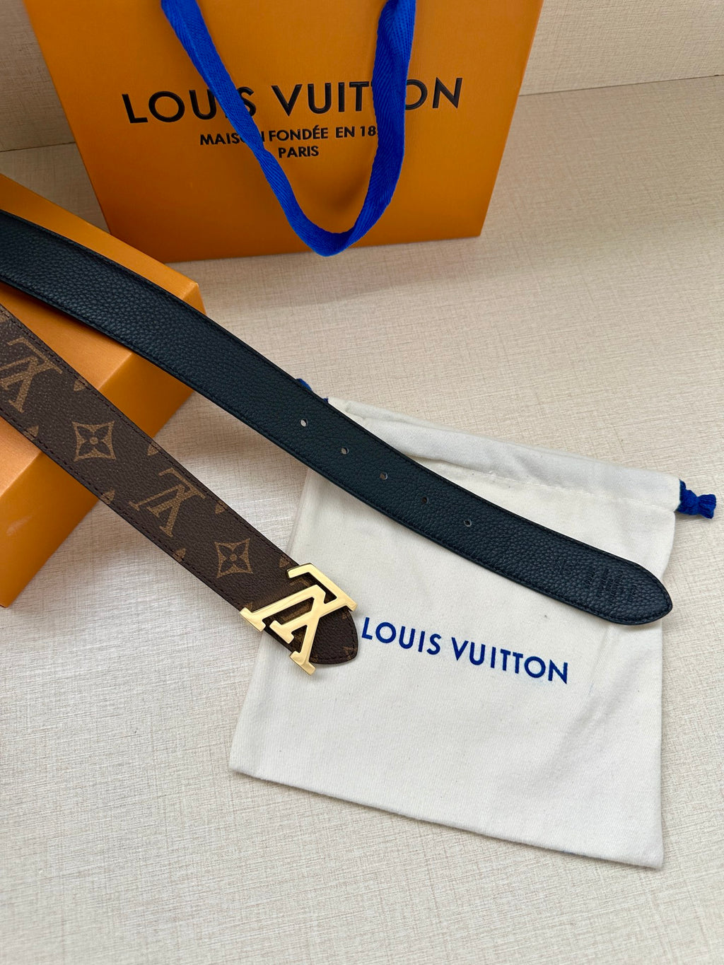 Navy leather belt with gold-tone buckle, monogram backing, on dust bag