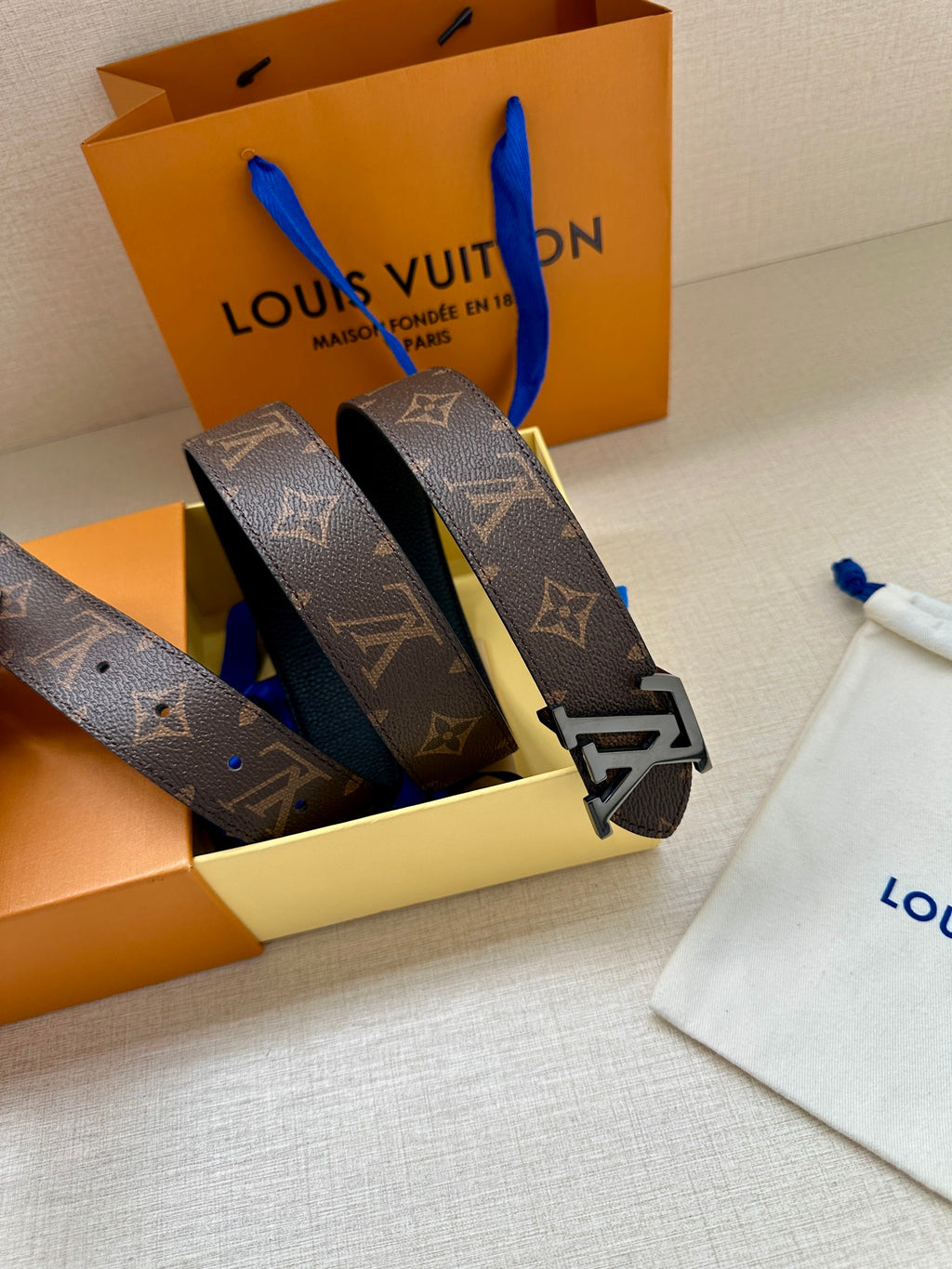 Monogram belt straps with gold-tone buckle placed on dust bag and gift box