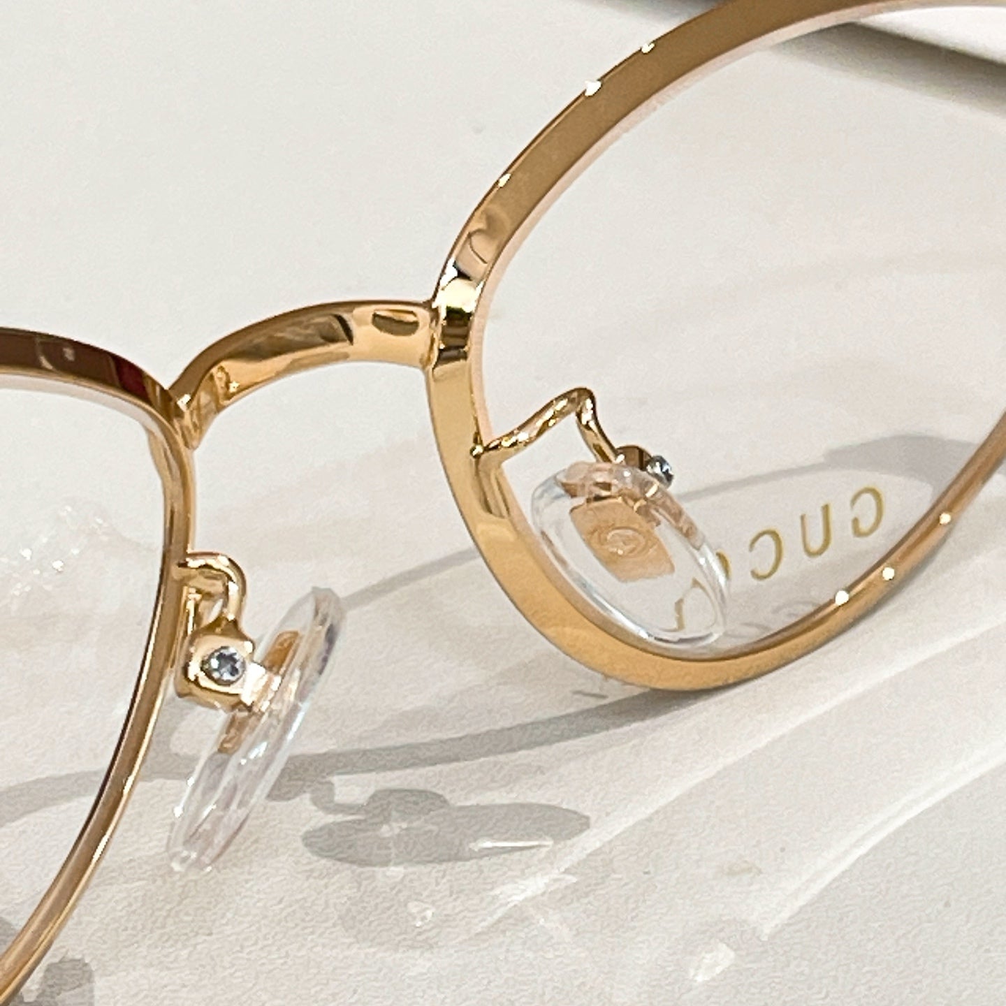 Gold eyeglass frame close-up with clear lens and hinge detail.