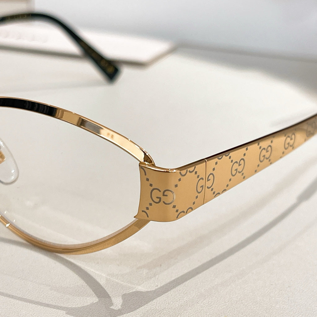 Gold eyeglass frame close-up with GG monogram temple and clear lens.