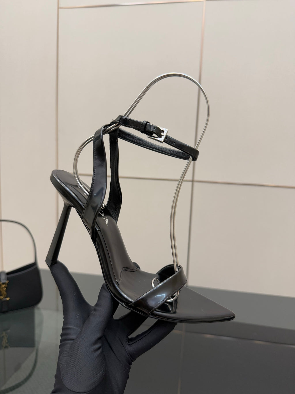 Black strappy high-heel sandal shown in hand, pointed toe and ankle strap