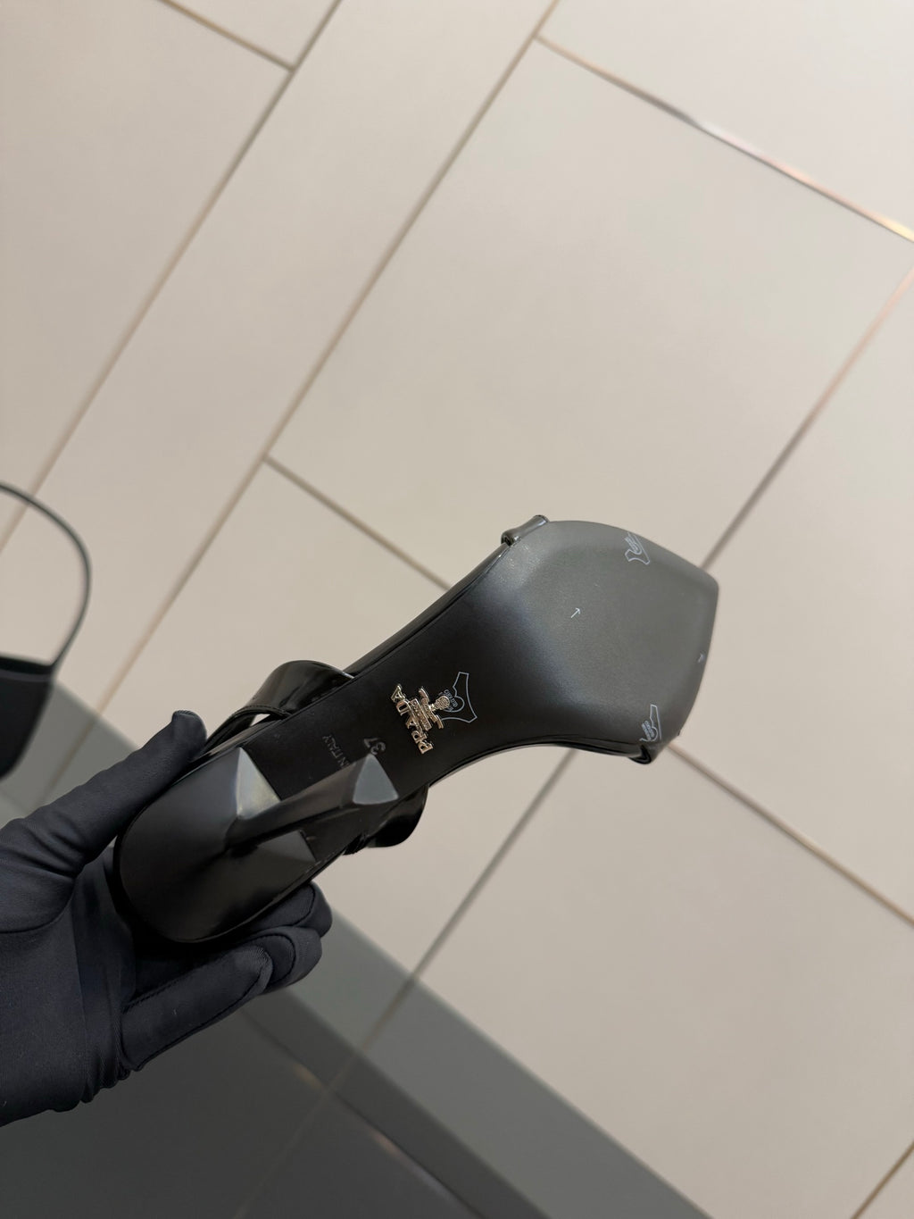 Black sandal heel cap with small embossed branding, held in gloved hand