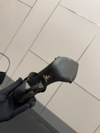 Black sandal heel cap with small embossed branding, held in gloved hand