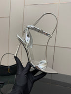 Prada women's metallic silver heeled sandals held by hand, side angle