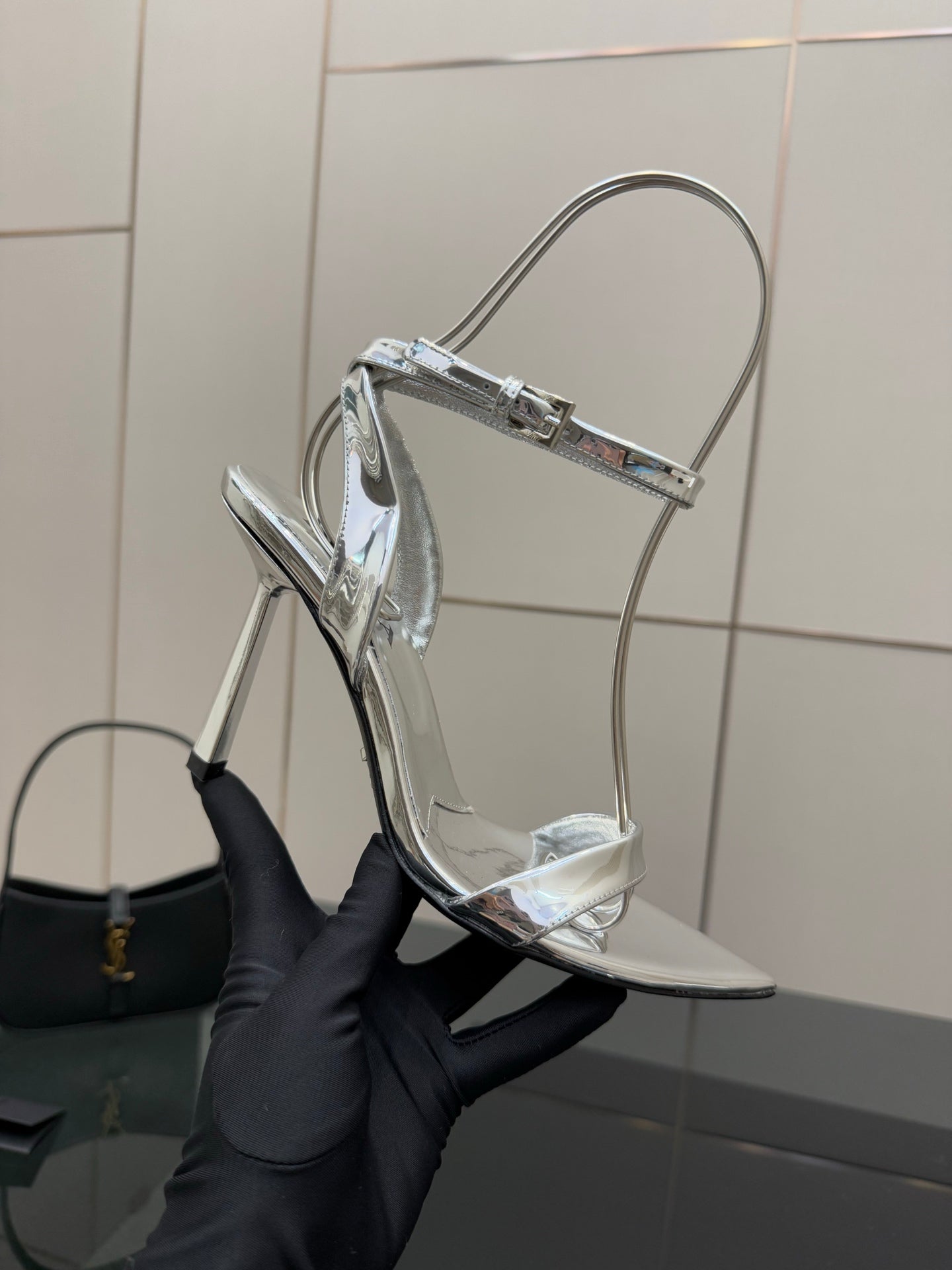Prada women's metallic silver heeled sandals held by hand, side angle