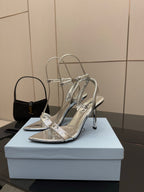 Prada women's metallic silver heeled sandals, front view on display stand