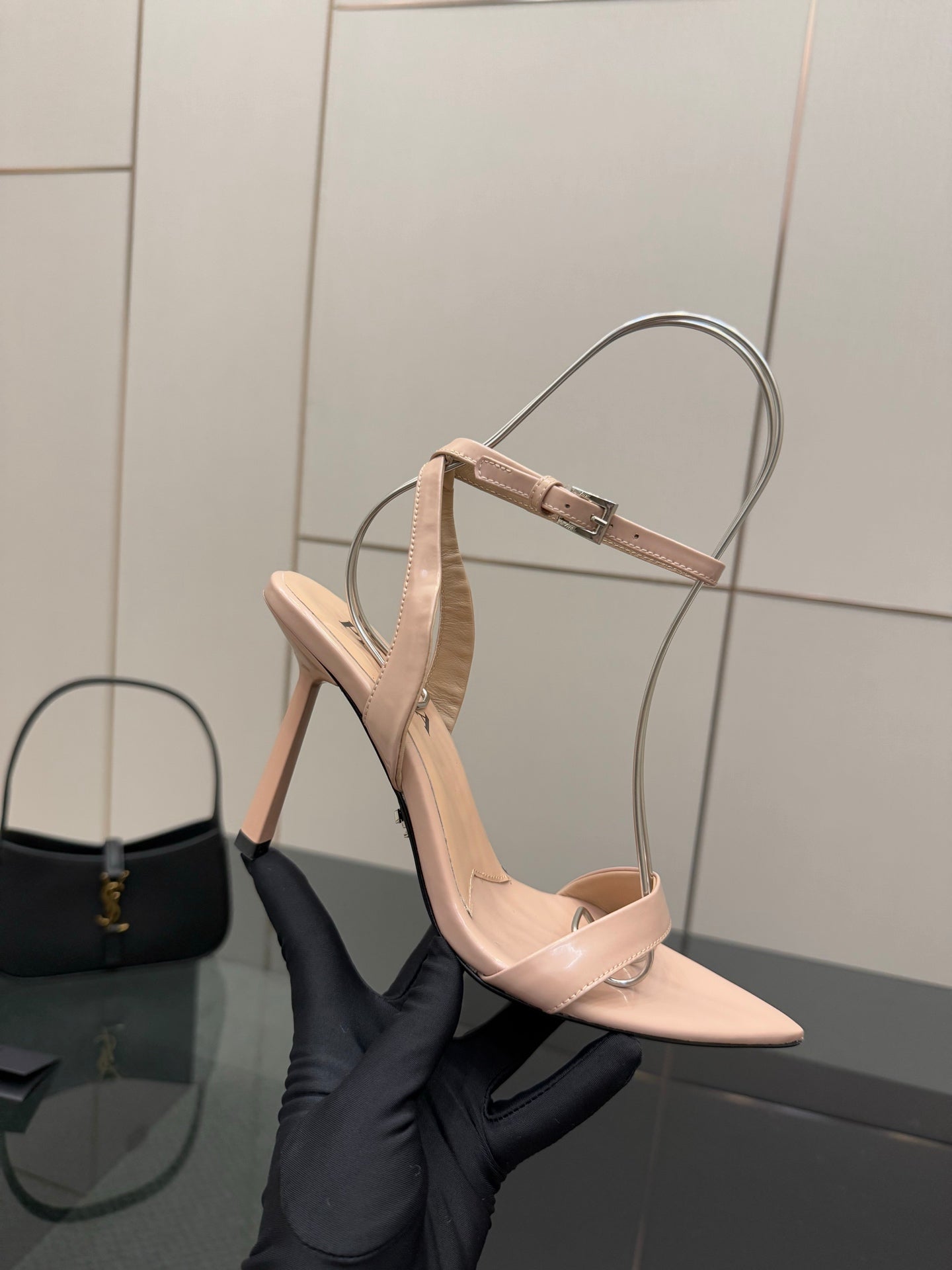 High-heel sandal in light nude with slingback strap and pointed toe, held in hand
