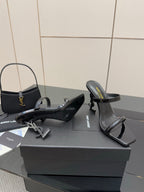 Black patent heeled mules with open toe and ankle strap, pair on shoe box