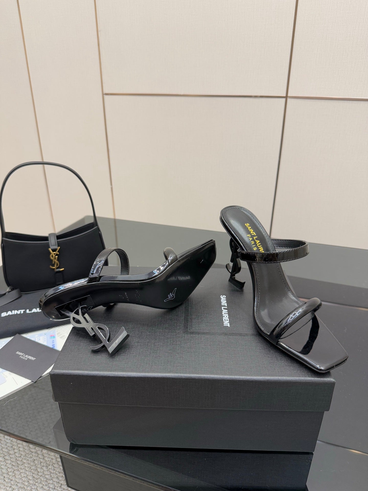 Black patent heeled mules with open toe and ankle strap, pair on shoe box