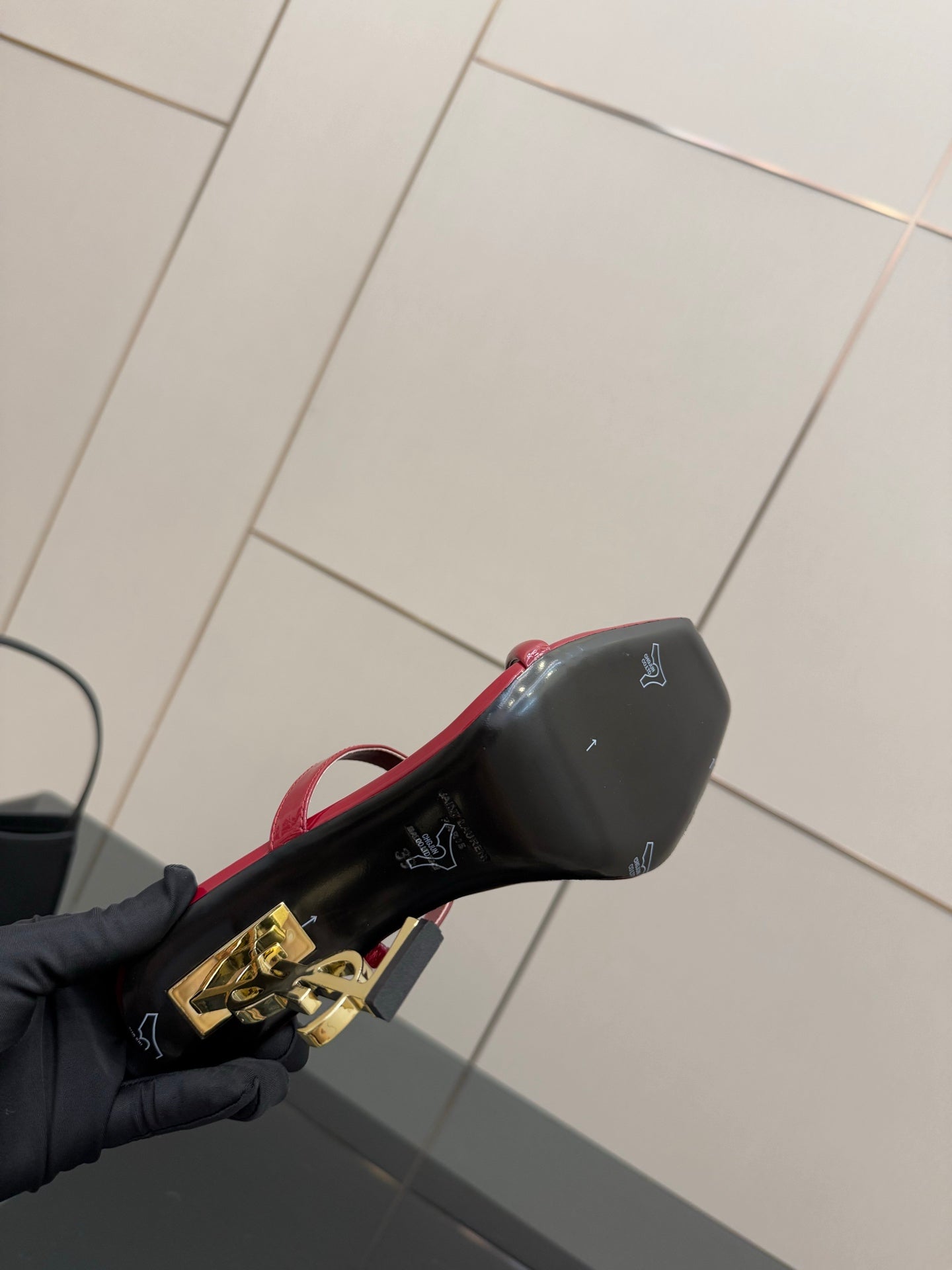 YSL ladies sandal heel close-up, gold YSL emblem on black heel and red strap