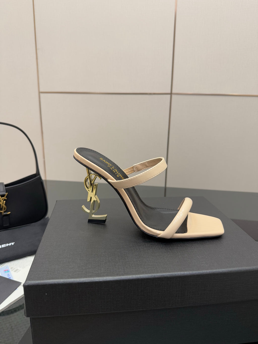 Two-tone heeled mule sandals with black lining, beige strap, and gold charm detail