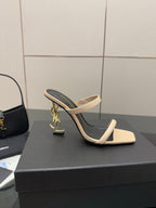 Two-tone heeled mule sandals with black lining, beige strap, and gold charm detail