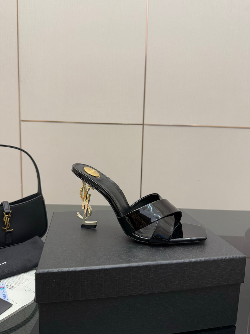 Black patent mule sandal with open toe strap and gold heel emblem