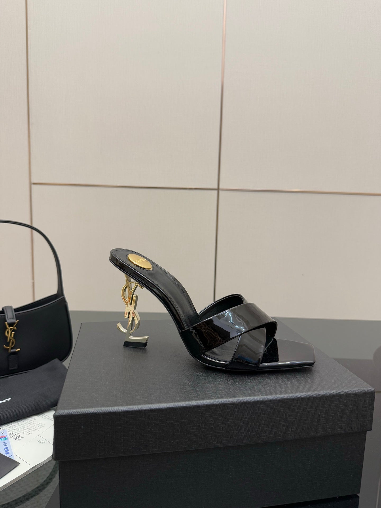 Black patent mule sandal with open toe strap and gold heel emblem