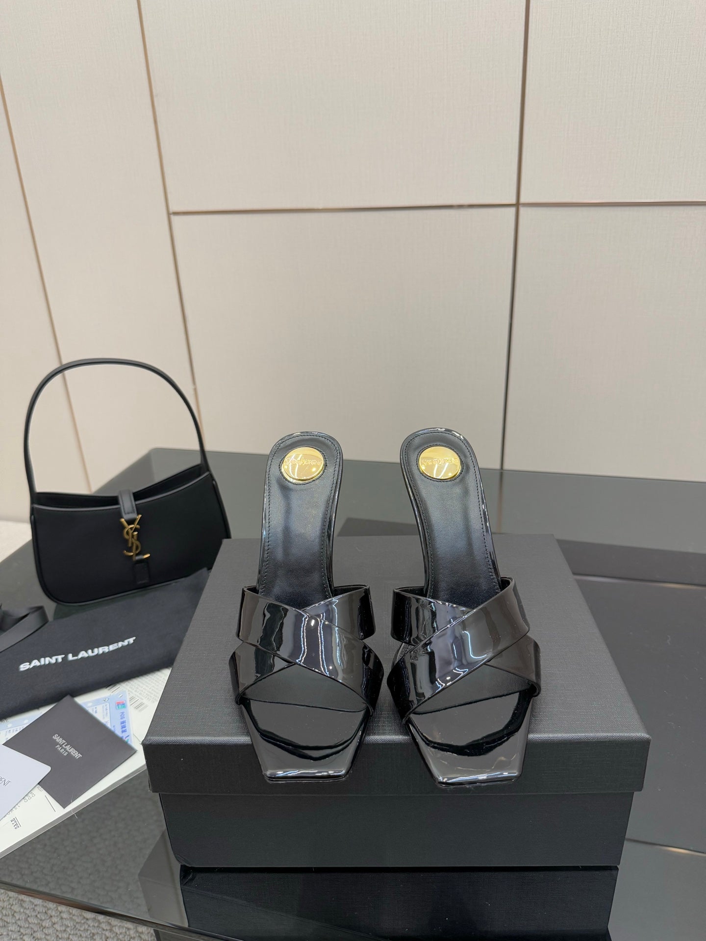 Black patent mule heels with open toe, platform base, and gold logo details