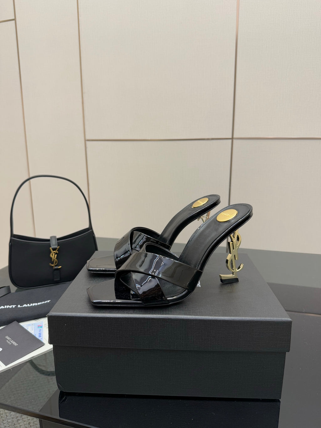 Black patent mule heels with open toe strap and gold Y-style logo at heel