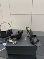Black heeled mule sandals with V-shaped crossover straps and gold logo heel hardware