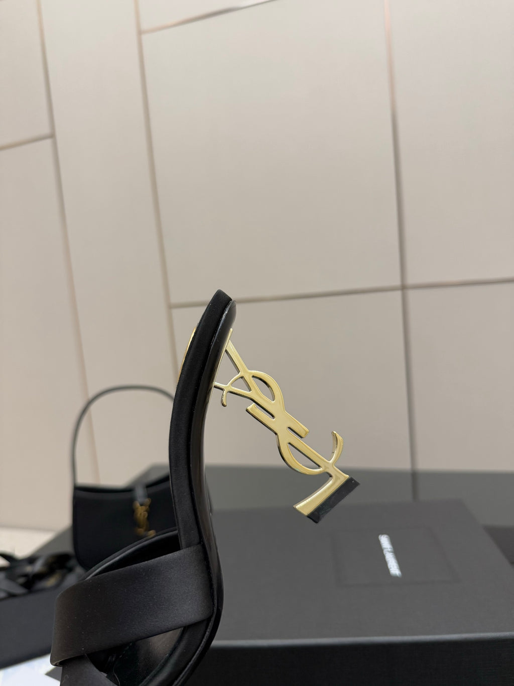 Side view of a black heeled mule sandal with gold YSL logo on the heel