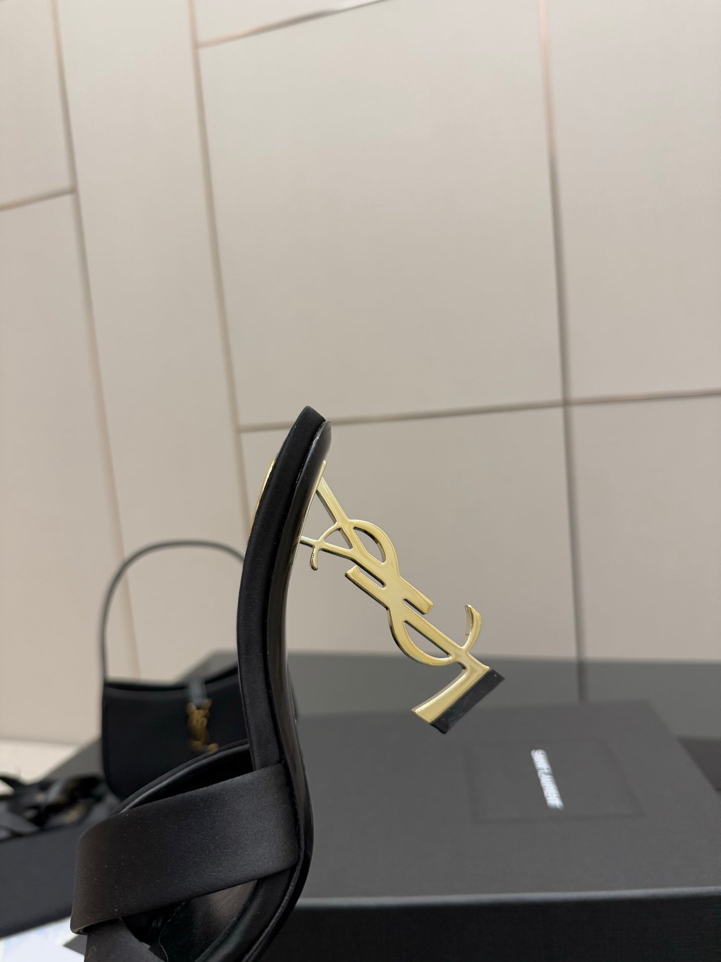 Side view of a black heeled mule sandal with gold YSL logo on the heel