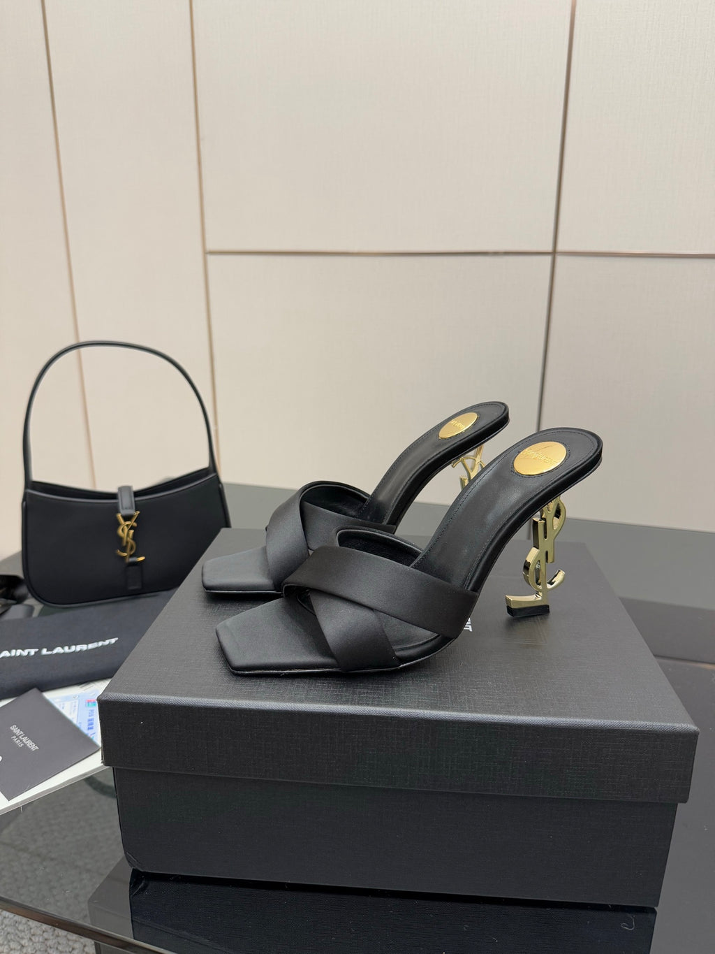 Pair of black heeled mule sandals with crossover strap design and gold YSL heel logos