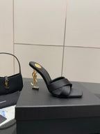 Black heeled mule sandal with crossover strap and gold YSL logo on the side of the heel