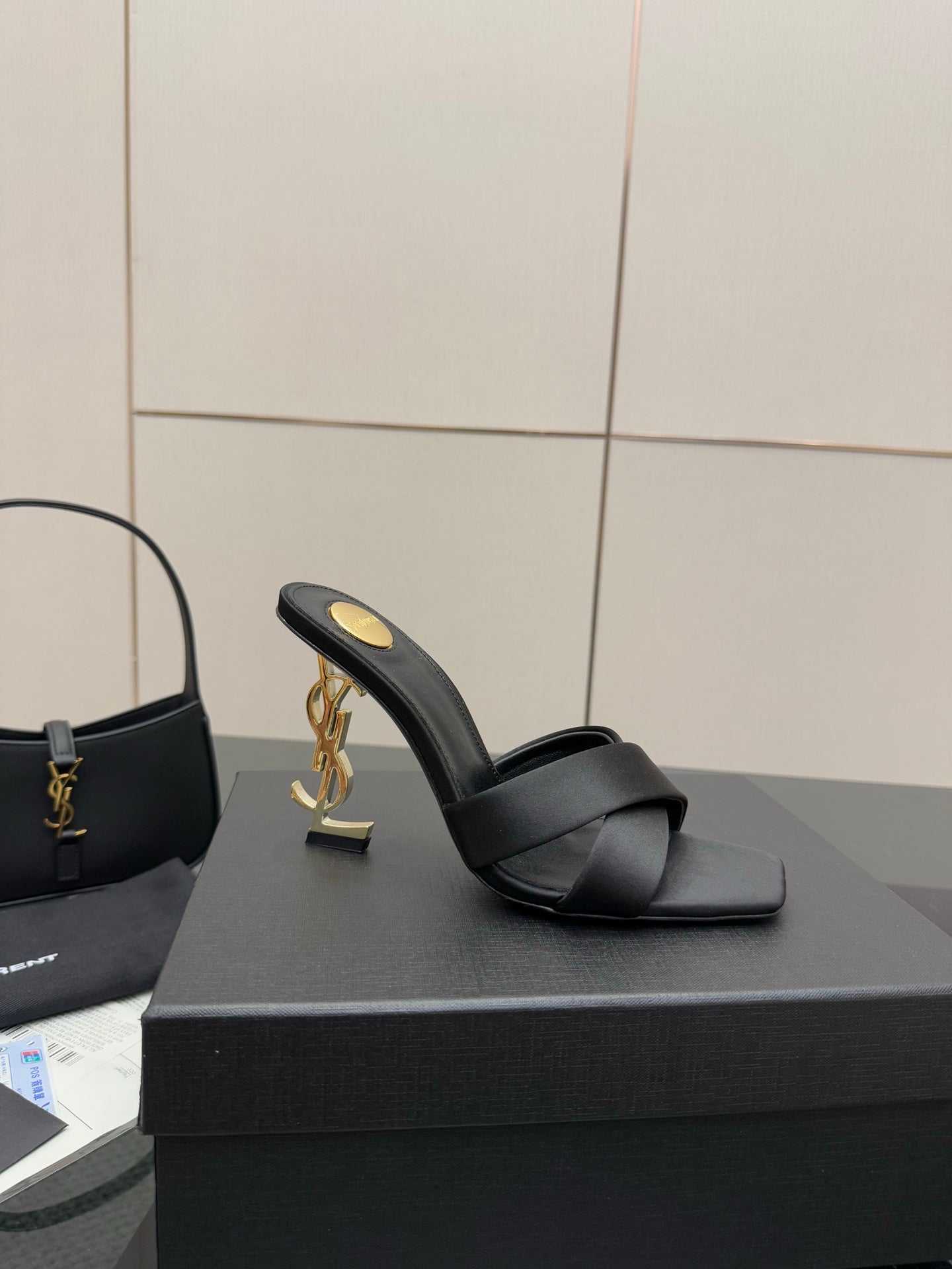 Black heeled mule sandal with crossover strap and gold YSL logo on the side of the heel
