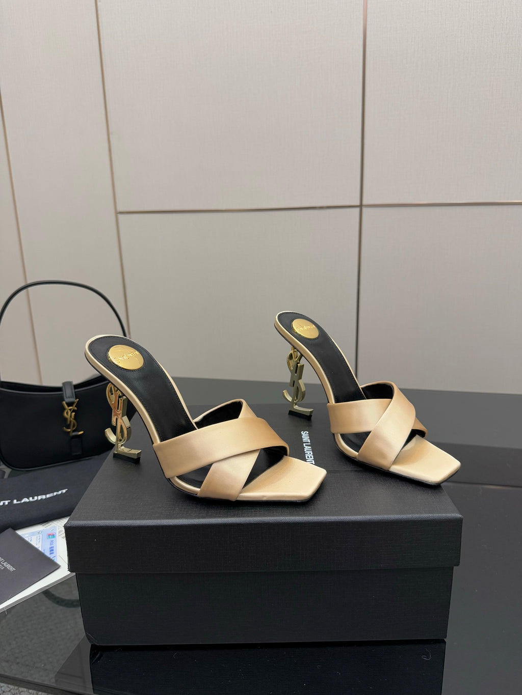 Cream heeled mule sandals with black sides and gold YSL logo detail, angled pair view.