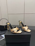 Cream heeled mule sandals with black sides and gold YSL logo detail, angled pair view.