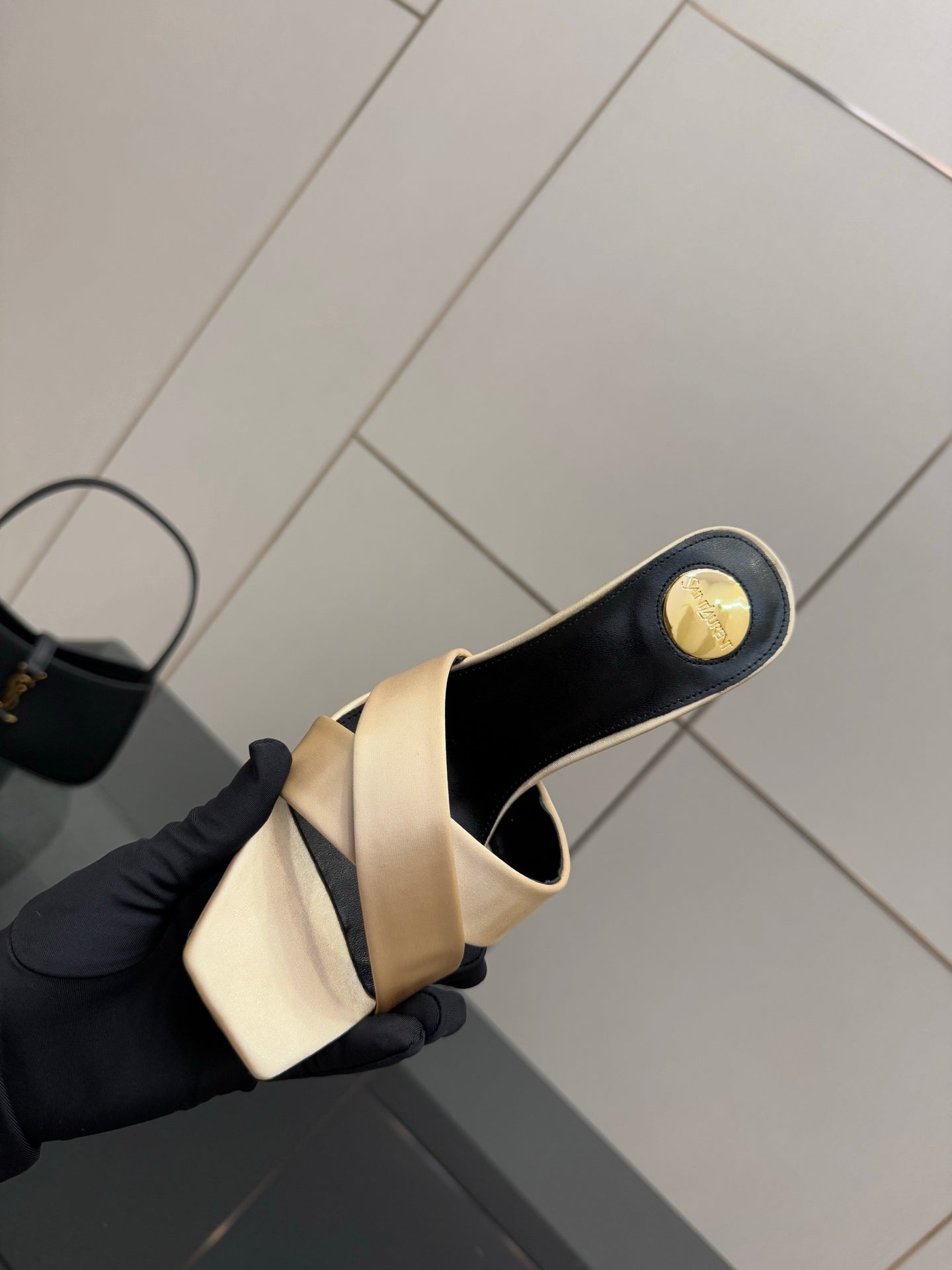 Cream heeled mule sandal with dark heel cap and gold YSL logo detail, angled top view.