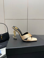 Cream heeled mule sandals with black outer edge and gold YSL logo on heel, side view.
