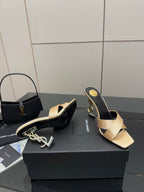 Cream and dark heeled mule sandals with gold YSL logo detail on heel, angled view.