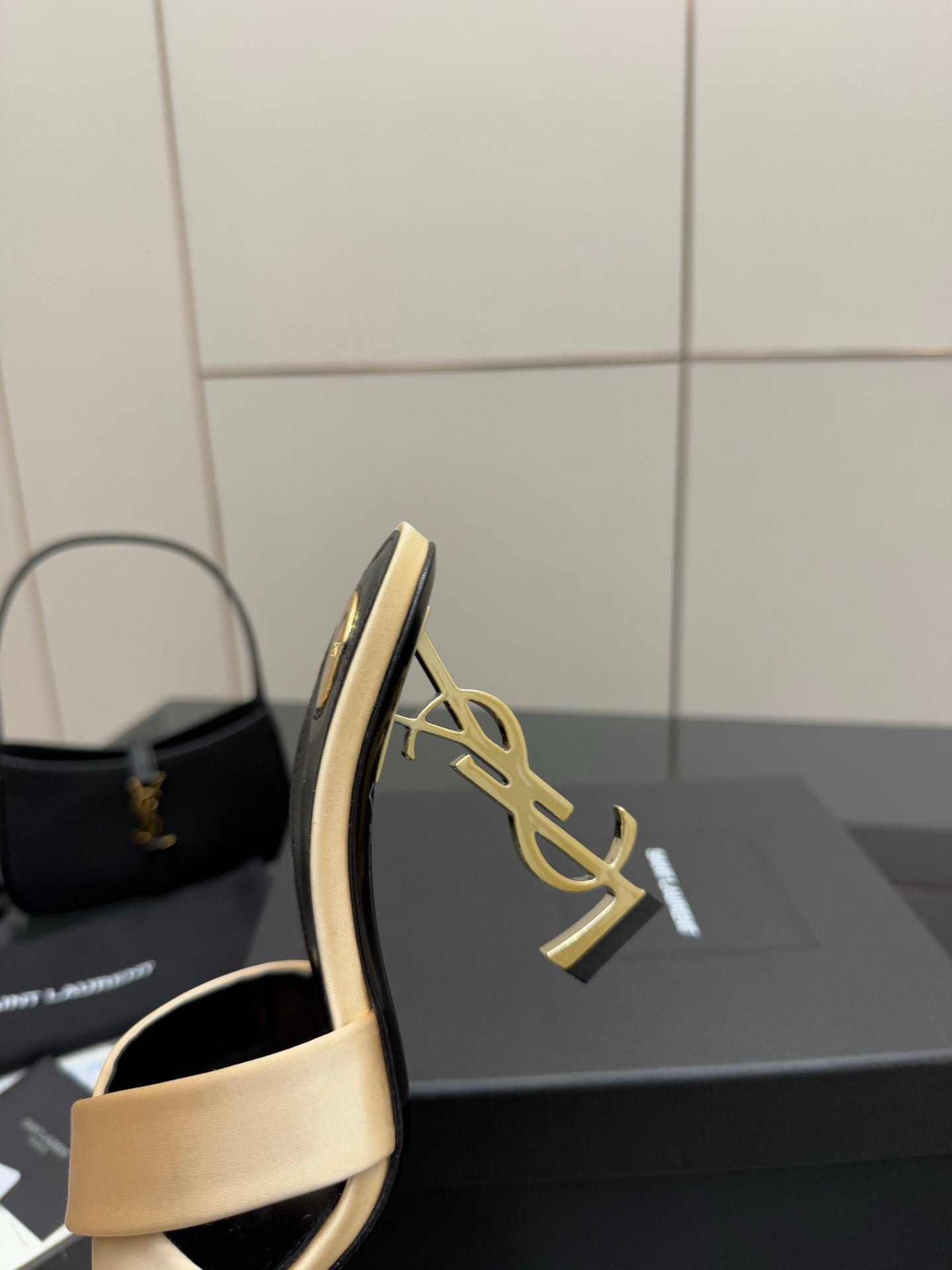 Heeled mule sandal with cream strap, dark sole, and gold YSL logo detail on heel.